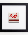 A framed matchbook with a white cover, featuring the red text "Ranch 616" and an underline in the shape of a lasso. The matchbook is centered inside a sleek, clear acrylic frame against a white background. This piece is known as Art Square Blk Frame by Match South.