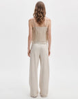 A woman with wavy, shoulder-length hair faces away, modeling Rag & Bone’s rb miramar trry drwcrd wde leg wide-leg jeans with a pull-on drawstring waistband and a beige spaghetti strap fitted top, against a plain white background.