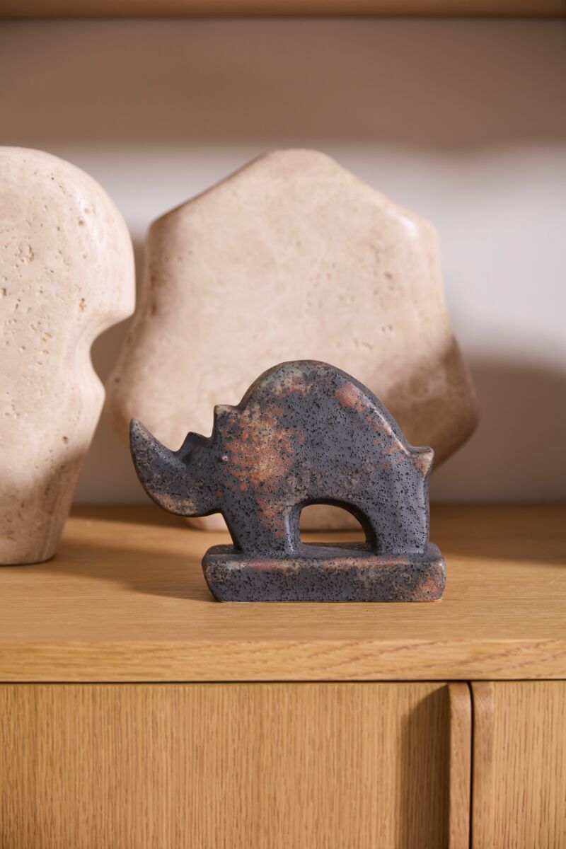 The Accent Decor Rhino Sculpture, a small dark figurine, rests on a wooden surface with two large cream-toned abstract ceramics behind it—an eye-catching home accent piece.