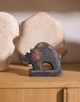 The Accent Decor Rhino Sculpture, a small dark figurine, rests on a wooden surface with two large cream-toned abstract ceramics behind it—an eye-catching home accent piece.