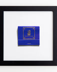 A framed display of a blue matchbook with gold accents, featuring "The Ritz-Carlton" logo and text. The matchbook is centered on a white background, surrounded by a sleek black frame that perfectly complements the elegant design, making it ideal for Match South's Art Square Blk Frame or other decorative pieces.