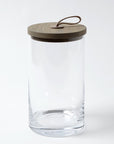 The Global Views BB-6.60025 Rustic Canister LG features clear glass, a flat wooden lid, and leather loop handle—perfect for adding Chalet Collection-inspired rustic charm to your kitchen. Shown on a plain white background.