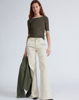 A woman wears the knit contrast ringer tee by Rag & Bone in olive green with cream high-waisted flared pants, holding a matching green jacket against a plain light background.