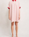 A person wearing the Denimist POLO SHIRT DRESS—loose-fitting with short sleeves, a spread collar, and red and white stripes—stands in white sandals against a plain background.