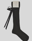 The Maria La Rosa College Velvet Bow Sock is a single black knee-high with vertical ribbing and a large velvet bow on the side, shown against a plain light background, featuring a white tag at the top.
