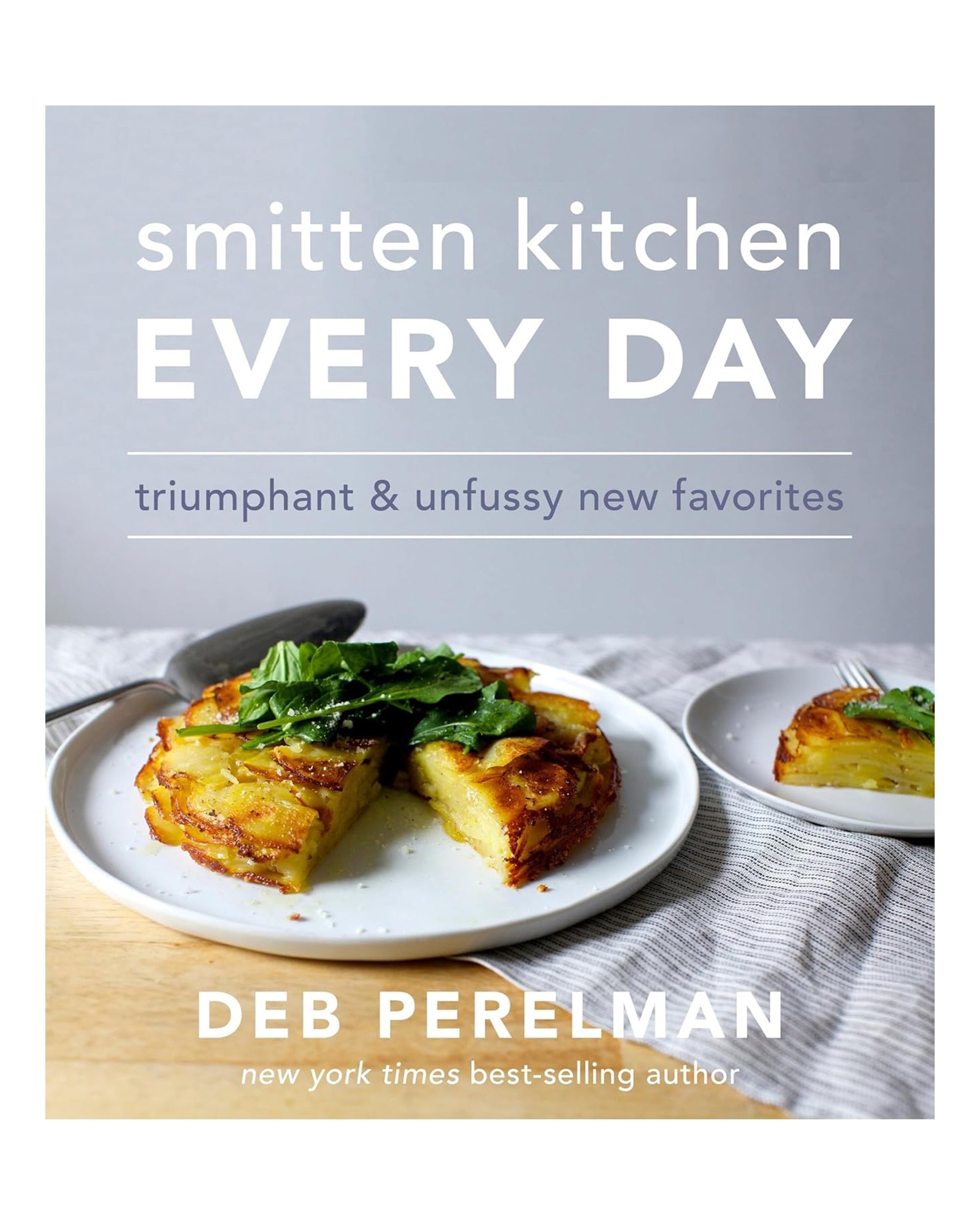 The cover of "Smitten Kitchen Every Day" by Random House shows golden potatoes topped with greens on a white surface. This cookbook offers simple recipes for tasty everyday meals.