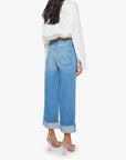 A woman with long dark hair wears Mother’s The Smoothie Crop Cuff high waisted light blue wide-leg jeans, a white blouse, and clear heels, shown from the back against a plain white background.