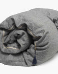 The Hedgehouse Throwbed is a rolled-up gray duvet with yellow stitching, a small dark blue tassel on one corner, and cotton-linen blend covers, shown on a plain white background.