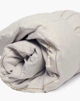 The Hedgehouse Throwbed, in light beige, is a neatly rolled cotton linen-blend comforter with a zipper and decorative tassel. Machine washable for easy care.