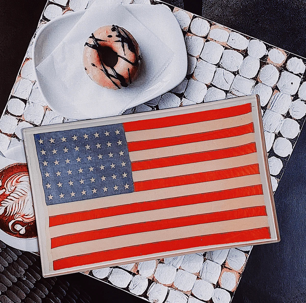 An artistic interpretation of the American flag on a Ben's Garden 5.5" x 8.5" tray, placed on a mosaic tiled surface in a Scottsdale, Arizona bungalow next to a white hat with a floral design.