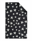 The Faire "Hand Towel : Into The Stars" is a black waffle weave microfiber towel with white stars in various sizes scattered across it and a small white corner tag.