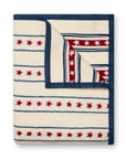 The Stars & Stripes Blanket by Faire features cream-colored fleece with blue edging, horizontal blue lines, and rows of red stars in a patriotic print—reversible for a similar look. Ideal for summer days by the New England seaside.