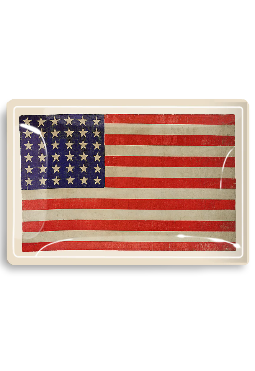 An aged American flag displayed in a glass frame, featuring 13 horizontal stripes and a blue canton with 50 stars, exhibiting a vintage aesthetic in a Scottsdale Arizona bungalow by Ben&#39;s Garden Tray 5.5&quot; x 8.5&quot;.