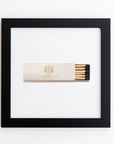 A minimalist artwork featuring a framed matchbox in the center. The matchbox, partially open to reveal a few matches, has "Stein Eriksen Lodge Deer Valley" text and logo on it. The frame is black with a white background, creating a stark contrast, all encased in clear acrylic for a sleek finish. This piece is part of the Art Square Blk Frame collection by Match South.