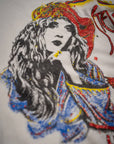 A close-up of a glittery woman illustration with wavy hair, in a patterned robe and hat, resting her chin on her hand. Printed on the Stevie Nicks Tee by Made Worn—a vintage unisex 90s-fit tee, handmade in Los Angeles.