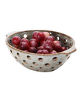 The Creative Co-op Berry Bowl with Glaze, featuring side handles and a reactive finish, displays fresh red grapes in style. Its pierced design makes it ideal for decorative use or rinsing fruit, shown here against a crisp white background.