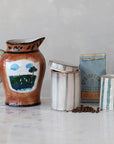 A hand-painted landscape jar, two Creative Co-op Striped Jars with Lid (one open), a blue Stumptown coffee bag, and scattered coffee beans rest on a marble surface.