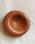The Faire Sumo Pocket Concrete Bowl, featuring a small, round, and smooth handmade design with thick edges, rests on a textured light fabric background, adding wabi sabi charm to your décor.