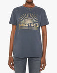 Someone wearing the Rowdy crewneck tee by Mother in dark gray with a gold sunburst and "SUNSET GOLD" on the front, styled oversized with blue jeans, layered necklaces, and bracelets. Made from 100% cotton for comfort.