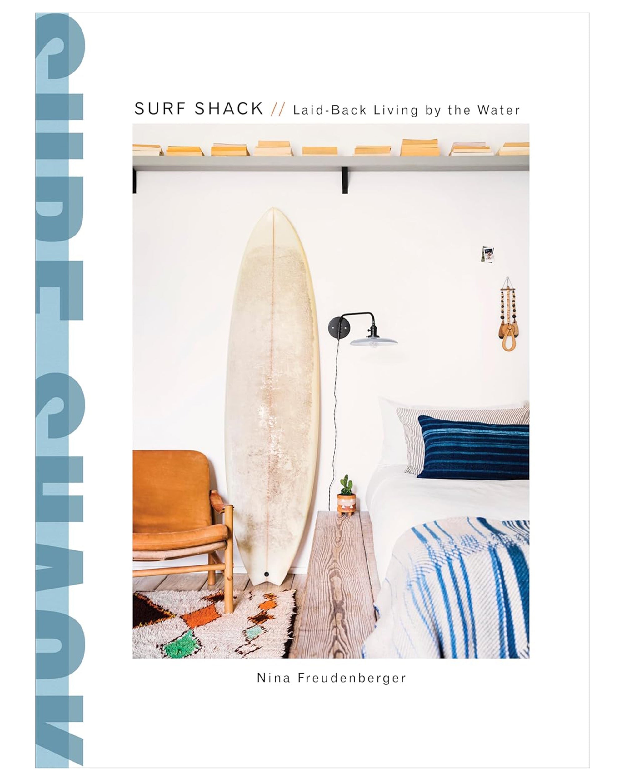 The book "Surf Shack //Laid Back Living By The Water" by Random House features inviting surfer-inspired interiors—surfboard, leather chair, and blue-pillowed bed—perfect for fans of casual coastal living.
