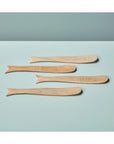 The Be Home 77-102 Sydney Whale Spreaders S/4, handcrafted from sustainably sourced mango wood and shaped like whales, are arranged on a light blue surface against a pale blue background.