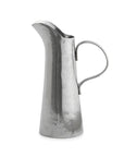 The VIN2270 Vintage Tall Tapered Pitcher by Faire is a tall, narrow silver pitcher with a curved handle and wide spout, hand made in Italy from artisan pewter with a subtly textured, smooth finish.