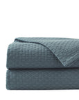 The Tegan Matelasse Coverlet by Eastern Accents, featuring a blue waffle-weave texture and mitered hem, is neatly folded and stacked against a plain white background.