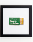 A framed print features an open box of matches labeled "Tennis matches". The box is green with a tennis ball graphic. The matchsticks have yellow tips, humorously playing on the idea of tennis matches. The clear acrylic frame adds a modern touch to this witty artwork by Match South, titled Art Square Blk Frame.