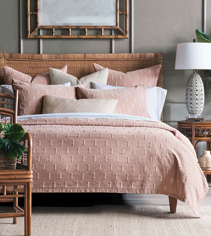 Sentence with replaced product:
Elegant bedroom with a rattan bed frame, blush pink bedding with a subtle pattern, white and beige pillows, and matching nightstands. A Bluff Euro 27x27" pillow from Eastern Accents, a large mirror, and ceramic table lamp complete the cozy Arizona-style setup.