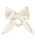The Silk Bow by Donni is a large, cream-colored 100% silk accessory with long, elegant tails, neatly tied and displayed against a plain white background.