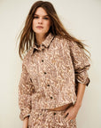 A woman with long brown hair wears BA&SH's Jacket Tullia, a light brown paisley-patterned 100% cotton denim piece, against a plain backdrop. For care, dry clean or use a high temperature iron.
