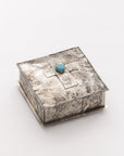 The 75-T-SL 6x6 SQ Silver Box w/ Dimples Cross by J Alexander Rustic Silver is a square, rustic hammered silver box with a raised cross and turquoise stone, ideal for Southwestern home decor.