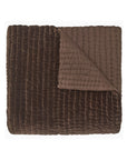 The John Robshaw Velvet Coverlet Queen is a folded, quilted brown blanket with a velvety texture and channel quilting; one corner is turned over, showing its smooth inner lining.