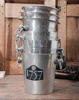 A stack of five Go Home Vintage Champagne Buckets with handles sits on a rustic wooden table; the top bucket features a "75 Henri Abelé" label.