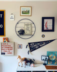 A wall featuring the Oxford Pennant "Do Right and Fear No Man" 18x24 camp flag, framed art, a ship model, a pirate hat, and a shelf with books, horse figurines, and an owl creates a whimsical, adventurous atmosphere.