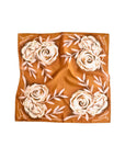 The Faire Wild Rag Silk Scarf features a warm brown background with cream floral patterns and pale leaf accents. Slightly wrinkled for a relaxed look, this silk and tencel scarf is a perfect cowgirl accessory.