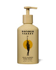 A beige pump bottle labeled "Faire Wild Garden Hand Wash" features a woman with wild herbs before a yellow circle, evoking cedar and botanical notes with its simple, modern design.