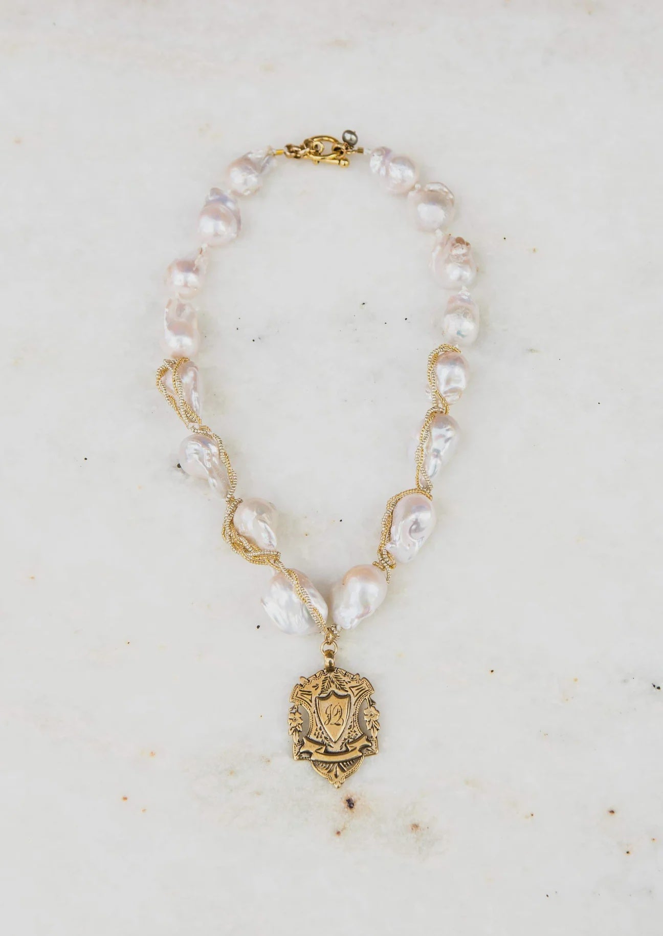 Elegant necklace featuring large baroque pearls interspersed with twisted gold links, centered by an Wrapped Ivory Pearl & Shield pendant displaying a vintage Arizona style, on a white marble background by Bittersweet Designs.