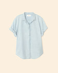 The Xirena Channing Shirt S25 in light blue cotton chambray features short sleeves, a collar, and rolled-up cuffs, displayed flat on a beige background.