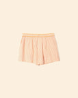 The Carlyn Short by Xirena features orange and white pencil stripes with a thicker orange stripe, an elasticized waistband, and is made from crisp cotton. The shorts are shown against a light beige background.