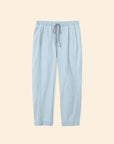 The Draper Pant by Xirena, shown flat on a beige background, features a light blue cotton chambray fabric, ankle-length cut, drawstring waist, and side seam pockets.