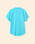 The Xirena Channing Shirt S25, in bright turquoise lightweight cotton chambray, is shown from the back on a beige background. Cuffed sleeves and a loose fit give it a cool, relaxed vibe.