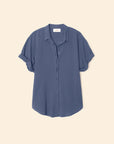 The Xirena Channing Shirt S25 is a loose-fitting, short-sleeve shirt in muted blue lightweight cotton chambray, shown on a light beige background with rolled sleeves for a relaxed vibe.