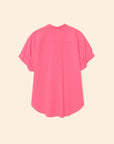 The Xirena Channing Shirt S25 in bright pink cotton chambray is shown from the back on a beige background, featuring rolled cuffs, a curved hem, and a hint of "boy meets girl" style.