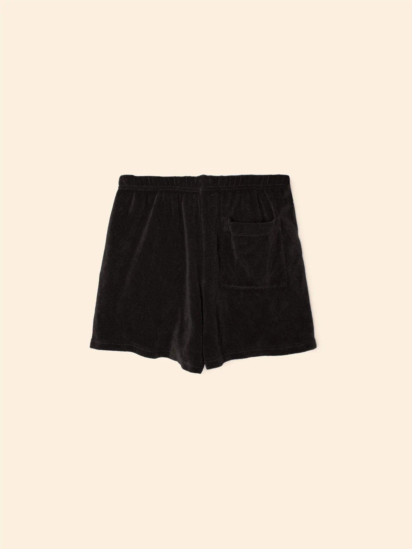 The Shayden Short by Xirena is a black terry cloth sweat short made from a soft cotton blend, featuring an elasticized waist and front patch pocket. Shown against a plain beige background.