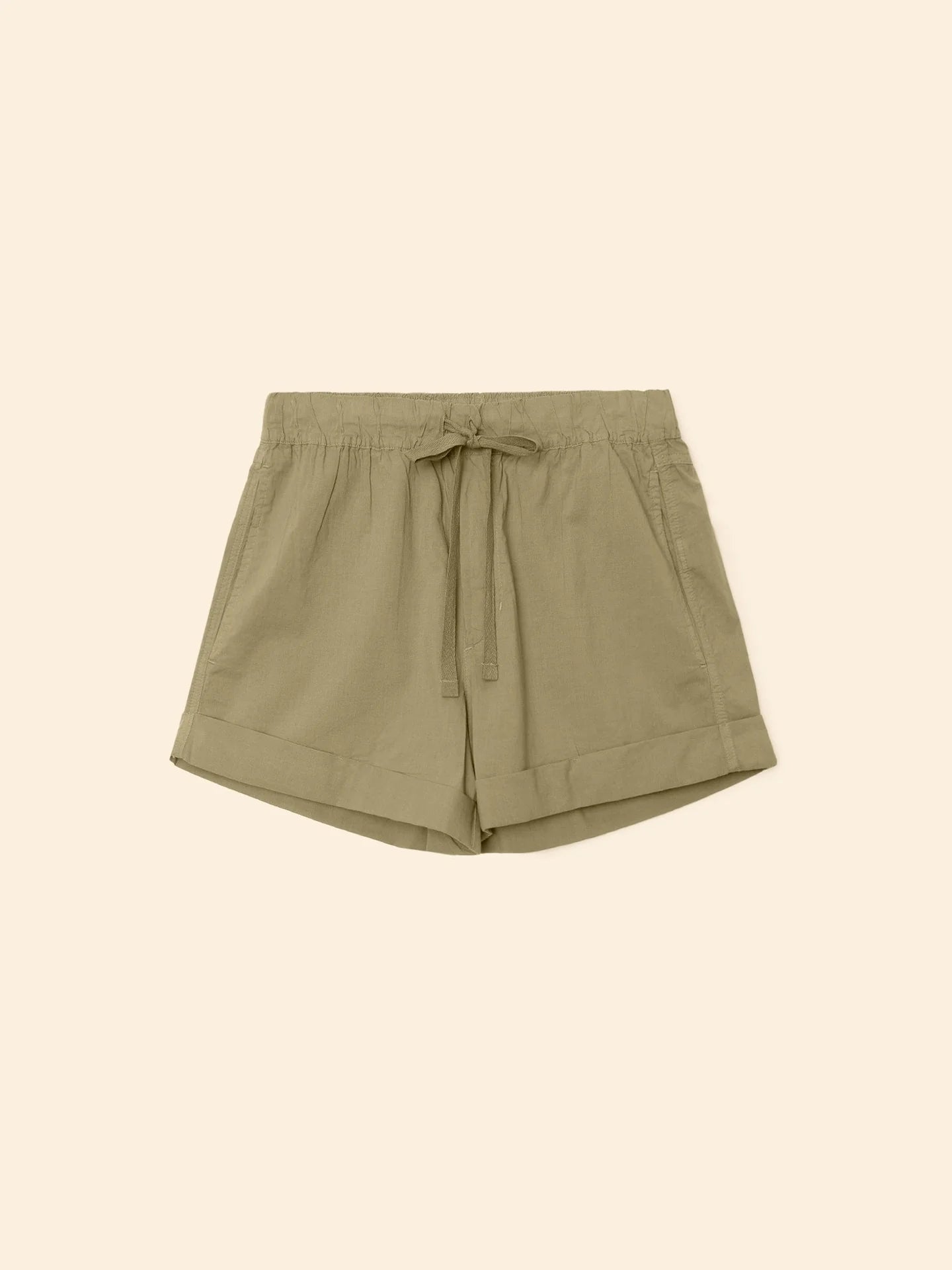 The Xirena Declan Short in light olive green cotton poplin features an elastic drawstring waist, side pockets, and cuffed hems, shown flat on a beige background.