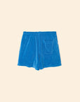 The Shayden Short by Xirena is a bright blue cotton-blend sweat short with an elastic waist and a single square front pocket, shown on a plain beige background.