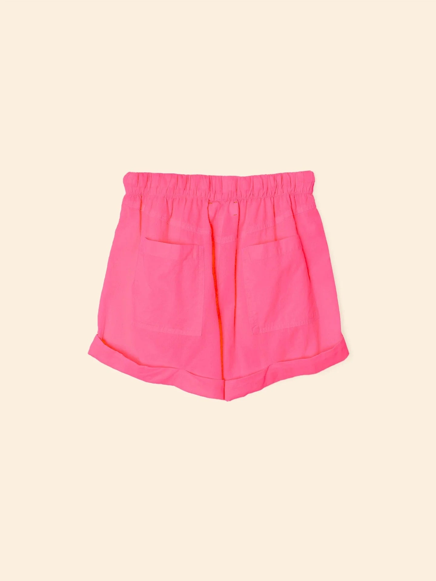 The Declan Short by Xirena features bright pink cotton poplin, an elasticized drawstring waist, two front pockets, and folded hems, shown against a plain light beige background.