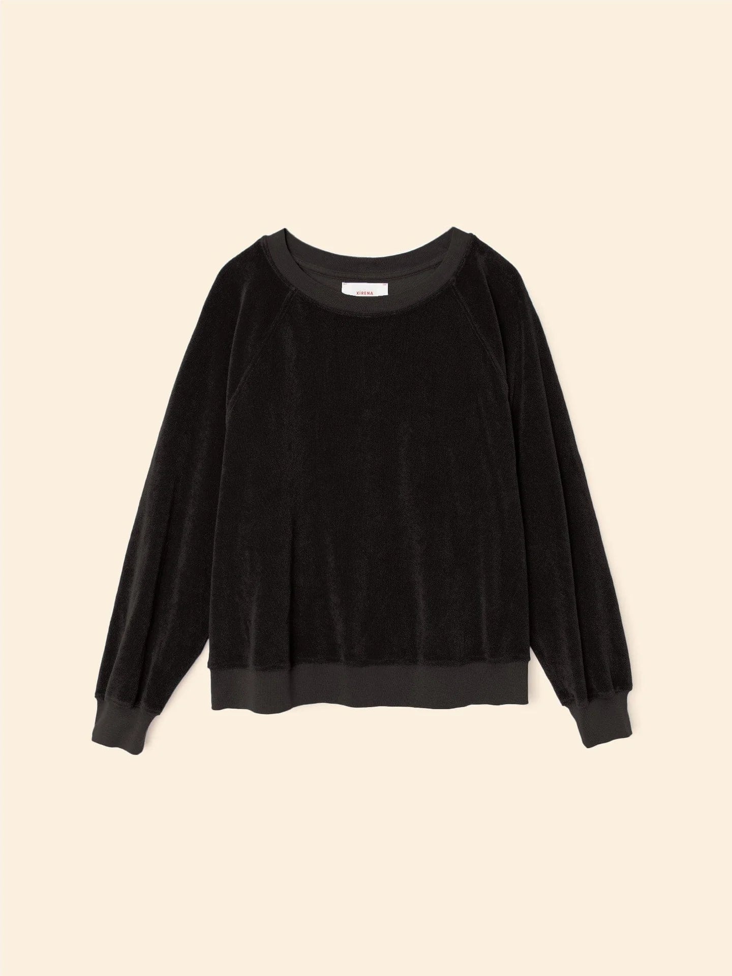 The Xirena Hopper Sweatshirt is a black long-sleeve pullover with a crew neck, ribbed cuffs and hem, made from a soft cotton blend velour, shown against a neutral beige background.