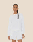A woman with braided hair models the Xirena Hopper Sweatshirt, a cotton blend piece, paired with matching white shorts against a plain beige background. Made in Los Angeles.